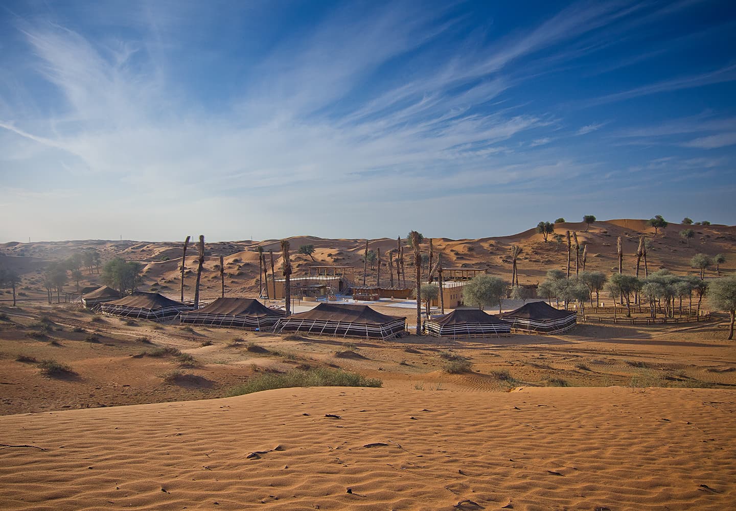 Golden sand dunes and a desert camp under a blue sky in Ras Al Khaimah